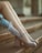 A pair of legs in sheer dotted socks and stylish high-heeled shoes are elegantly displayed on stone steps. The wearer also dons delicate gloves, adorned with a pearl ring, which adds a touch of vintage charm to the ensemble.