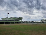A modern green building with a distinctive roof design set against a backdrop of cloudy skies. It is situated in a grassy area with a flagpole displaying the Philippine flag.