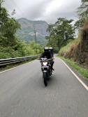 Action shot of riders cruising along a winding road framed by lush greenery under a bright blue sky.