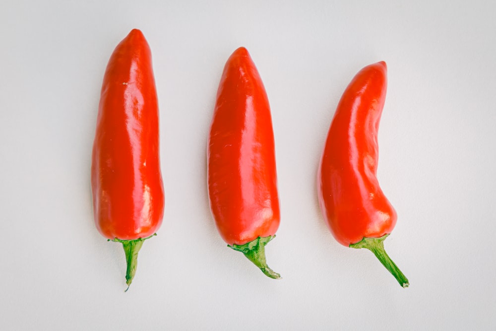 three red hot peppers on a white surface