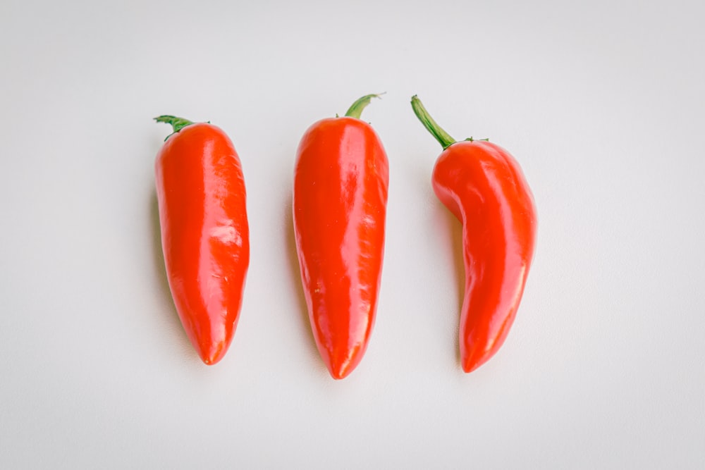 three red hot peppers on a white surface