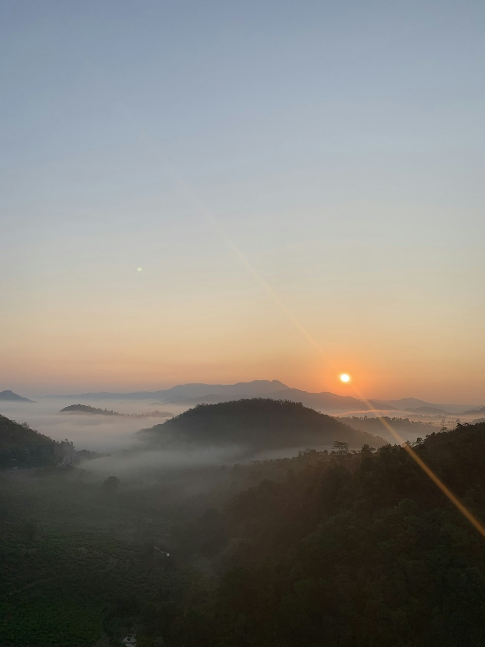 the sun is setting over the mountains in the fog