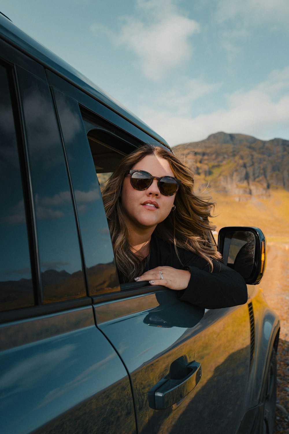 uma mulher usando óculos escuros inclinada para fora da janela de um carro