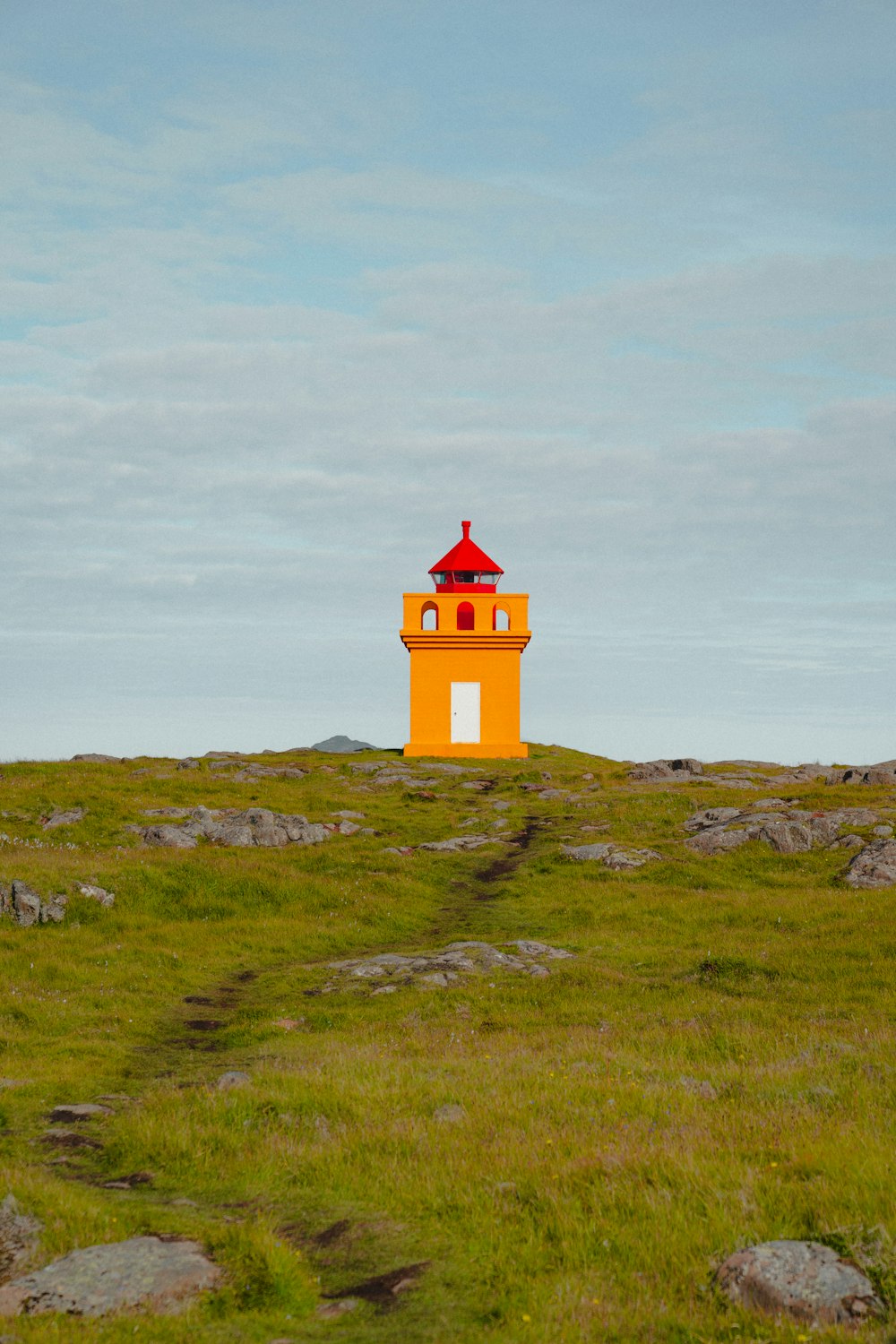 a yellow and red light house sitting on top of a hill