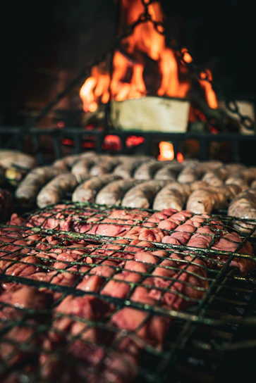 A vibrant, close-up shot of sizzling grilled meats and chorizos on a rustic barbecue grill.