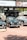 A collection of classic cars is displayed outdoors on a brick-paved area. Behind the cars, there is a banner with 'Sotheby's' and other automotive images. The cars, polished and well-maintained, include a green car in the center with a distinctive front grill, flanked by other vintage vehicles.
