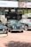 A collection of classic cars is displayed outdoors on a brick-paved area. Behind the cars, there is a banner with 'Sotheby's' and other automotive images. The cars, polished and well-maintained, include a green car in the center with a distinctive front grill, flanked by other vintage vehicles.