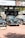 A selection of classic cars displayed outdoors on a brick platform, beneath a large Sotheby's auction sign. The scene includes a row of well-maintained vintage vehicles, including green and black models, with a background of promotional banners for a luxury online automotive auction.