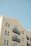 An apartment building with cream-colored siding features multiple windows and black balcony railings against a clear blue sky. The building has a clean and modern architectural style with symmetrical windows and neatly arranged balconies.
