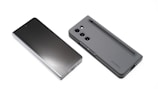 Two modern smartphones are displayed on a white background. One phone lies flat with its screen facing upward, showcasing a sleek, reflective surface. The other phone, seen from the back, features a matte case with a camera module and a stylus inserted into a slot.