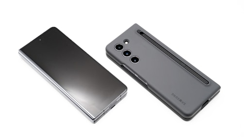 Two modern smartphones are displayed on a white background. One phone lies flat with its screen facing upward, showcasing a sleek, reflective surface. The other phone, seen from the back, features a matte case with a camera module and a stylus inserted into a slot.