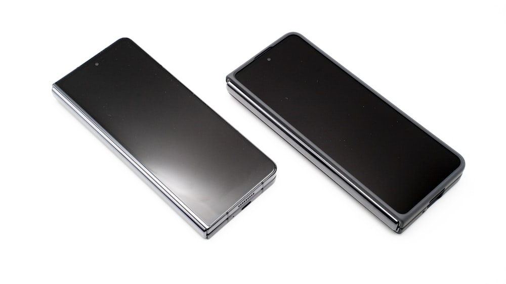 흰색 표면에 나란히 있는 두 개의 검은색 휴대폰