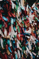 A vibrant array of multicolored ribbons tightly packed together, creating a textured and lively pattern. The ribbons are primarily in shades of red, blue, green, white, and gold, with varied lengths and arrangements.