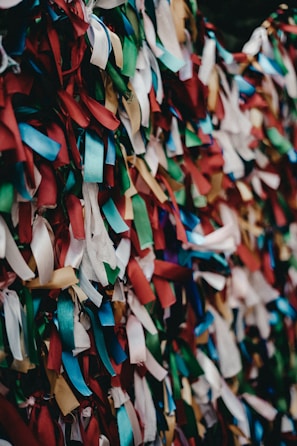 A vibrant array of multicolored ribbons tightly packed together, creating a textured and lively pattern. The ribbons are primarily in shades of red, blue, green, white, and gold, with varied lengths and arrangements.