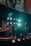 A band performing on stage with various musical instruments, including a keyboard, drum set, and electric guitar. The stage is illuminated by multiple bright lights, creating a vibrant atmosphere. Band members are engaged in playing their instruments, contributing to a dynamic live music setting.