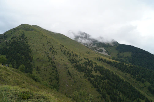 A group of travelers hiking through lush green mountains with mist rolling over the peaks.
