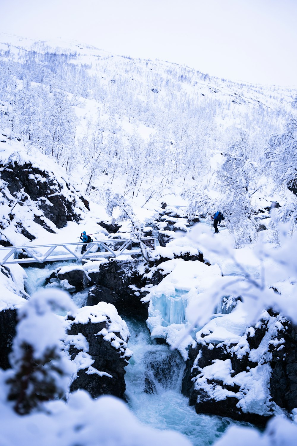 a man walking across a snow covered bridge over a river