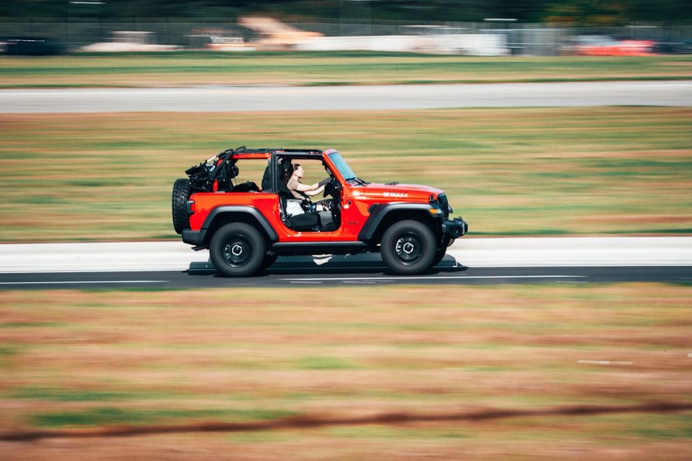 a red jeep driving down a road next to a field