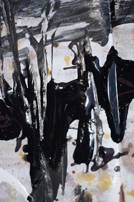 Abstract expressionist artwork featuring bold, dark brushstrokes on a textured background with shades of white, black, and hints of gold and red. The composition creates a dynamic and chaotic pattern, with drips and splatters adding depth and movement.