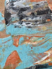 An abstract painting featuring swirling patterns and dynamic brushstrokes. The composition includes patches of light turquoise, earthy orange, white, black, and subtle hints of red and yellow. The colors blend together with a textured surface, creating an energetic and vibrant appearance.