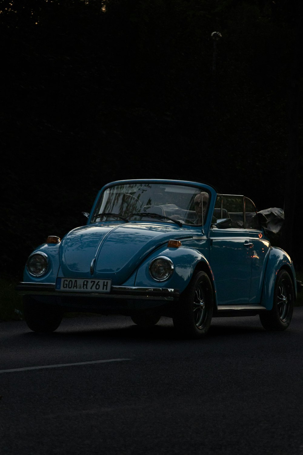 a blue car driving down a street next to a forest