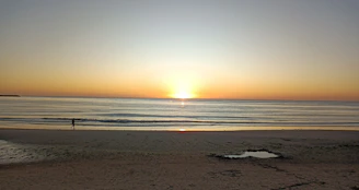 A serene sunrise over a calm beach with a lone traveler enjoying the view.
