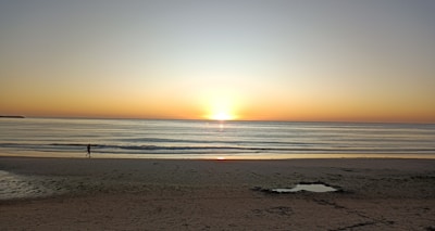 A vibrant sunrise over a tropical beach with a lone traveler walking along the shore, symbolizing new journeys.