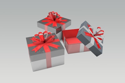 Three gift boxes with red ribbons and bows are arranged on a smooth gradient background. Two boxes are closed, while the third is open, revealing a red interior. The boxes are silver and white, contrasting with the vivid red ribbons.