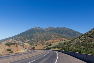 A winding highway surrounded by lush green hills under a clear blue sky.
