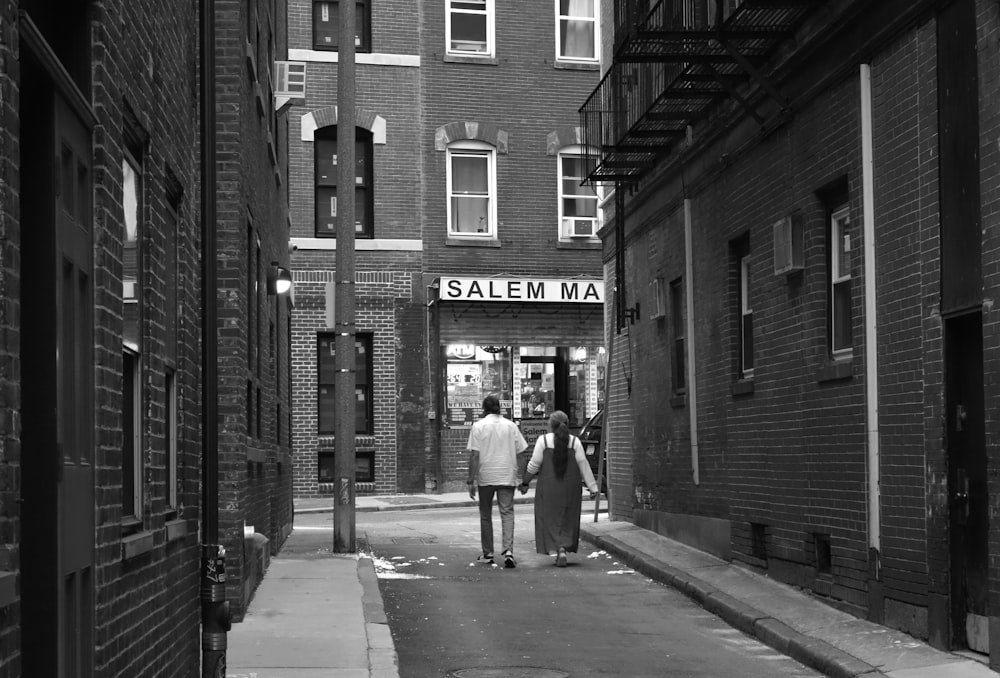 a couple of people walking down a street next to tall buildings