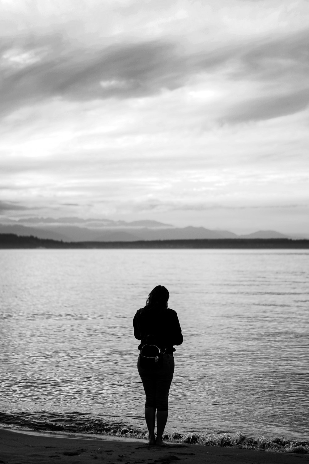 uma mulher em pé em uma praia ao lado de um corpo de água