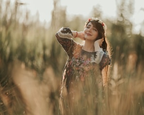 A young woman wearing a colorful, flowy dress standing in a sunlit meadow surrounded by wildflowers.