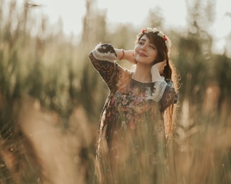 A young woman wearing a colorful, flowy dress standing in a sunlit meadow surrounded by wildflowers.