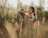 A joyful young woman wearing a flowing boho dress standing in a sunlit meadow.