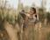 A joyful young woman wearing a flowing boho dress standing in a sunlit meadow.