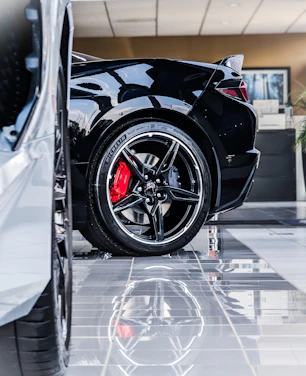 Close-up of sleek alloy wheels on a luxury sports car in a dark showroom with subtle red lighting accents.
