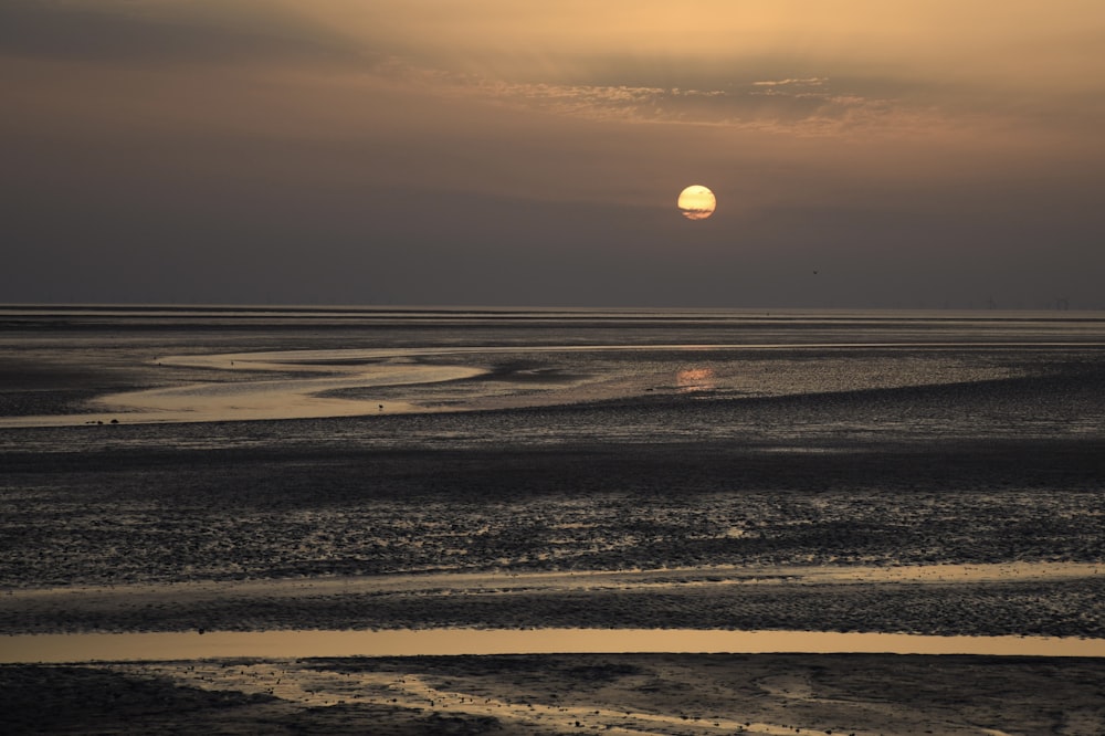 the sun is setting over the ocean on a cloudy day