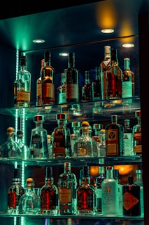 A contemporary home bar unit featuring built-in shelves stocked with colorful bottles and ambient LED lighting.