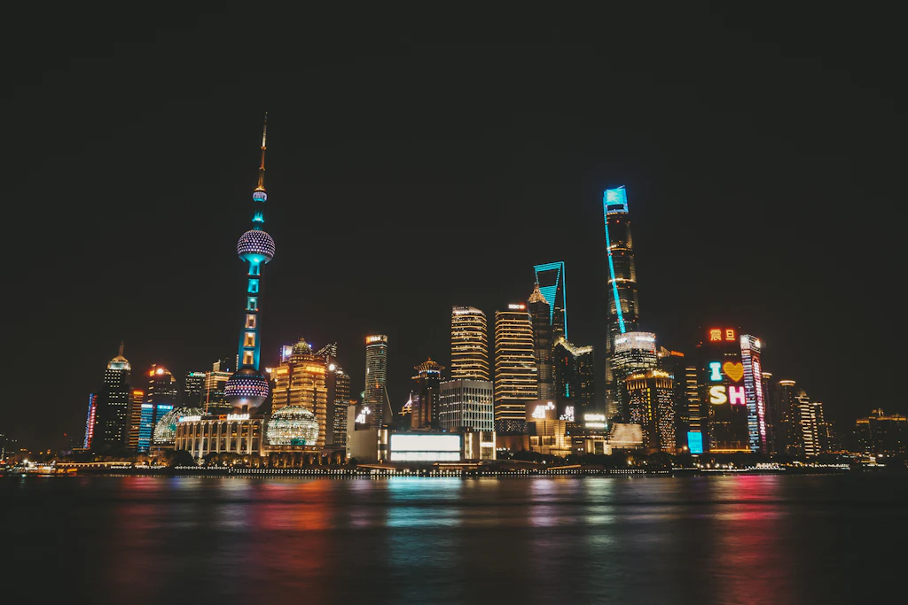 The lit Shanghai skyline across the Huangpu River at night, reflected in the water