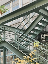 An outdoor metal staircase leading to a contemporary building surrounded by greenery.