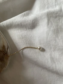 A minimalist pendant hanging delicately on a thin chain, set against a soft white background.