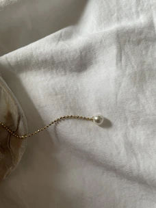 A slender gold chain catching the light as it drapes softly over a cream-colored silk cloth.