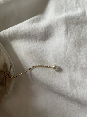 A slender gold chain catching the light as it drapes softly over a cream-colored silk cloth.