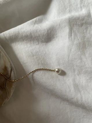 Close-up of a delicate gold chain resting on soft white fabric, catching the light beautifully.