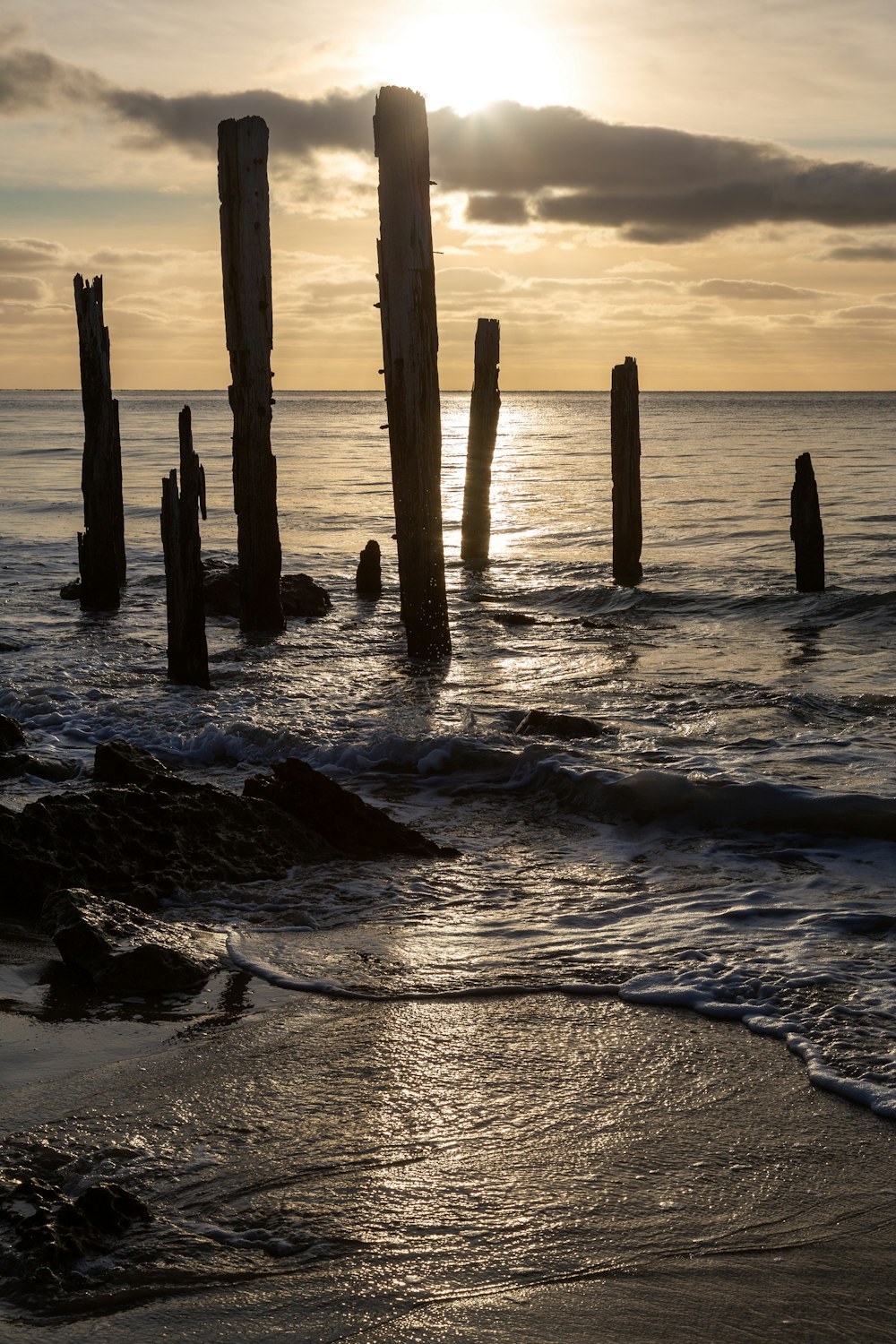 the sun is setting over the ocean with old wooden posts sticking out of the water