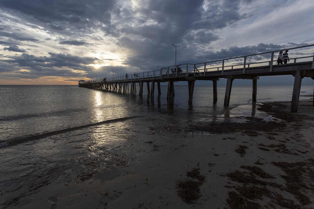 a pier that is next to the ocean under a cloudy sky