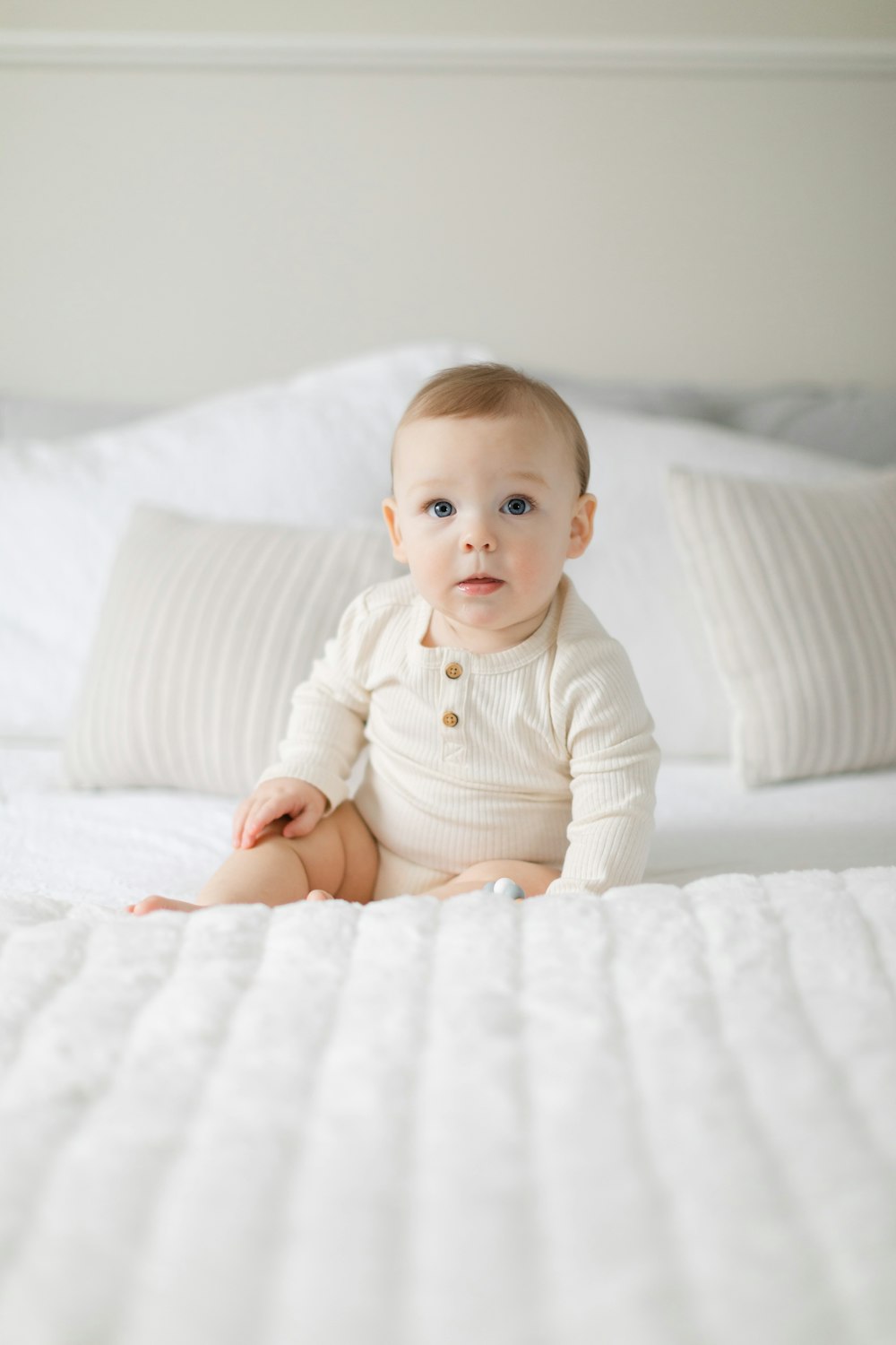 a baby sitting on a bed with white sheets