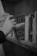 A hand is reaching for a book on a wooden bookshelf. The book's cover displays the name 'Susan Hill', and it appears to be a sequel related to 'Rebecca.' Other books are also visible on the shelf, with different titles and colors, but are mostly obscured. The setting is cozy and suggests a library or a personal study.