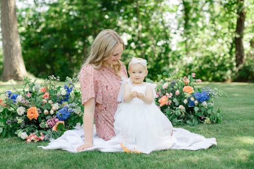 A mother and daughter sharing a quiet moment in a garden filled with pink and gold flowers.
