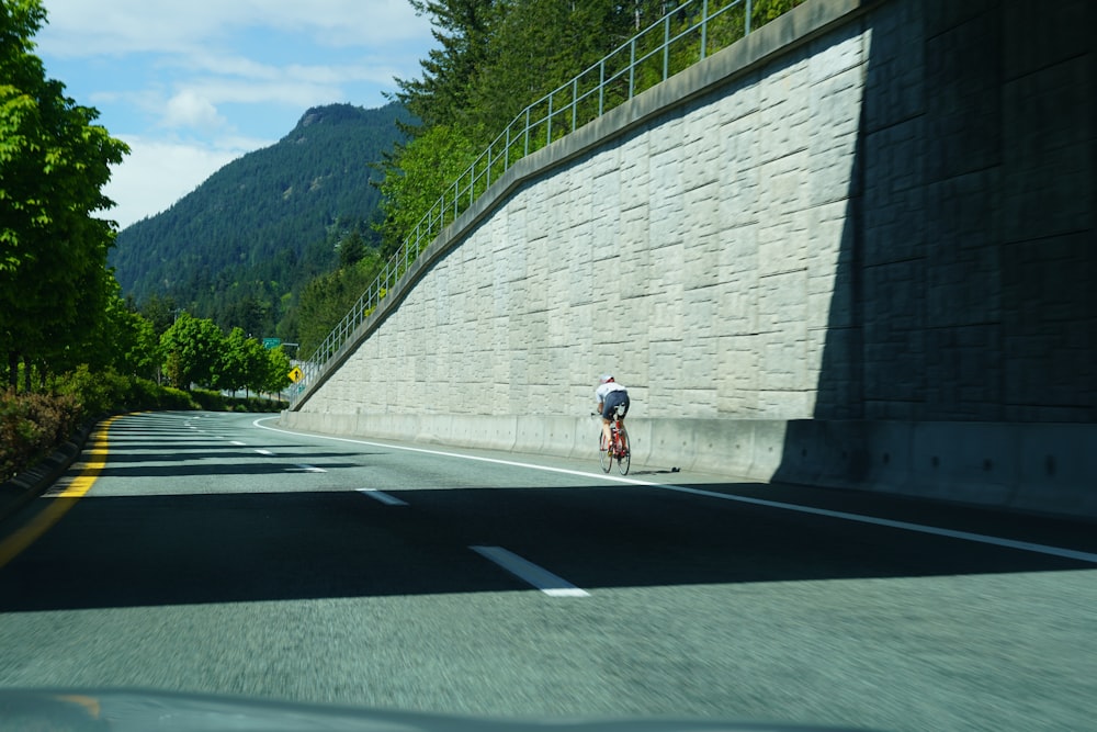 a man riding a bike down a street next to a stone wall